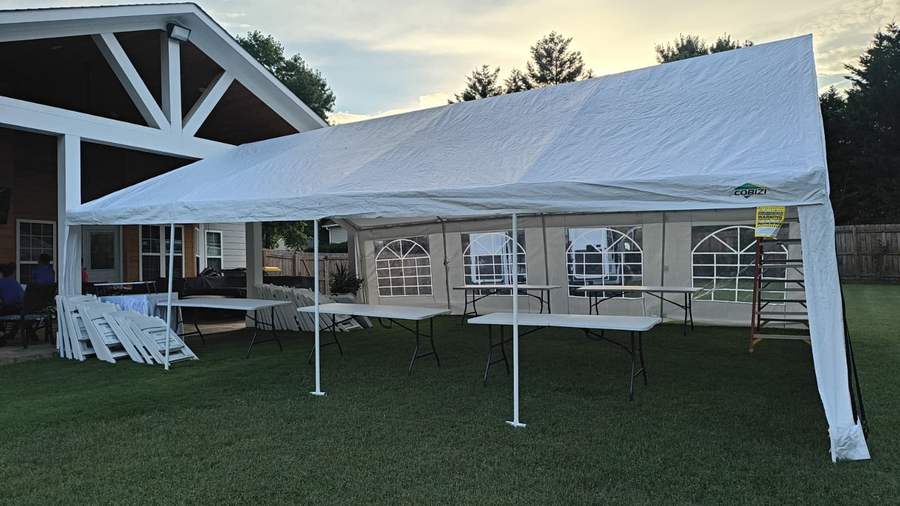 White tent with sidewalls, tables and chairs set on a back lawn