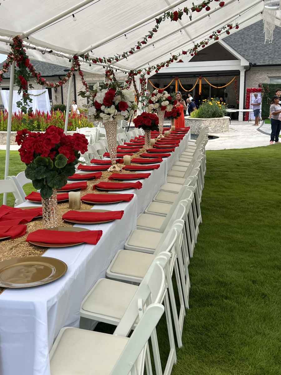 Long banquet table with red rose centerpieces and gold chargers under a tent