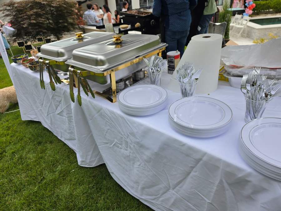 Chafing dishes, plates and cutlery arranged on a linen buffet table
